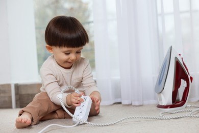 Photo of Little boy playing with iron plug and power strip at home. Child in danger