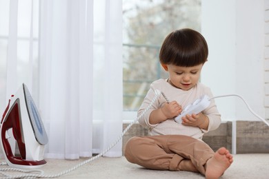 Photo of Little boy playing with iron plug and power strip at home. Child in danger