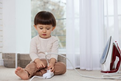 Photo of Little boy playing with iron plug and power strip at home. Child in danger