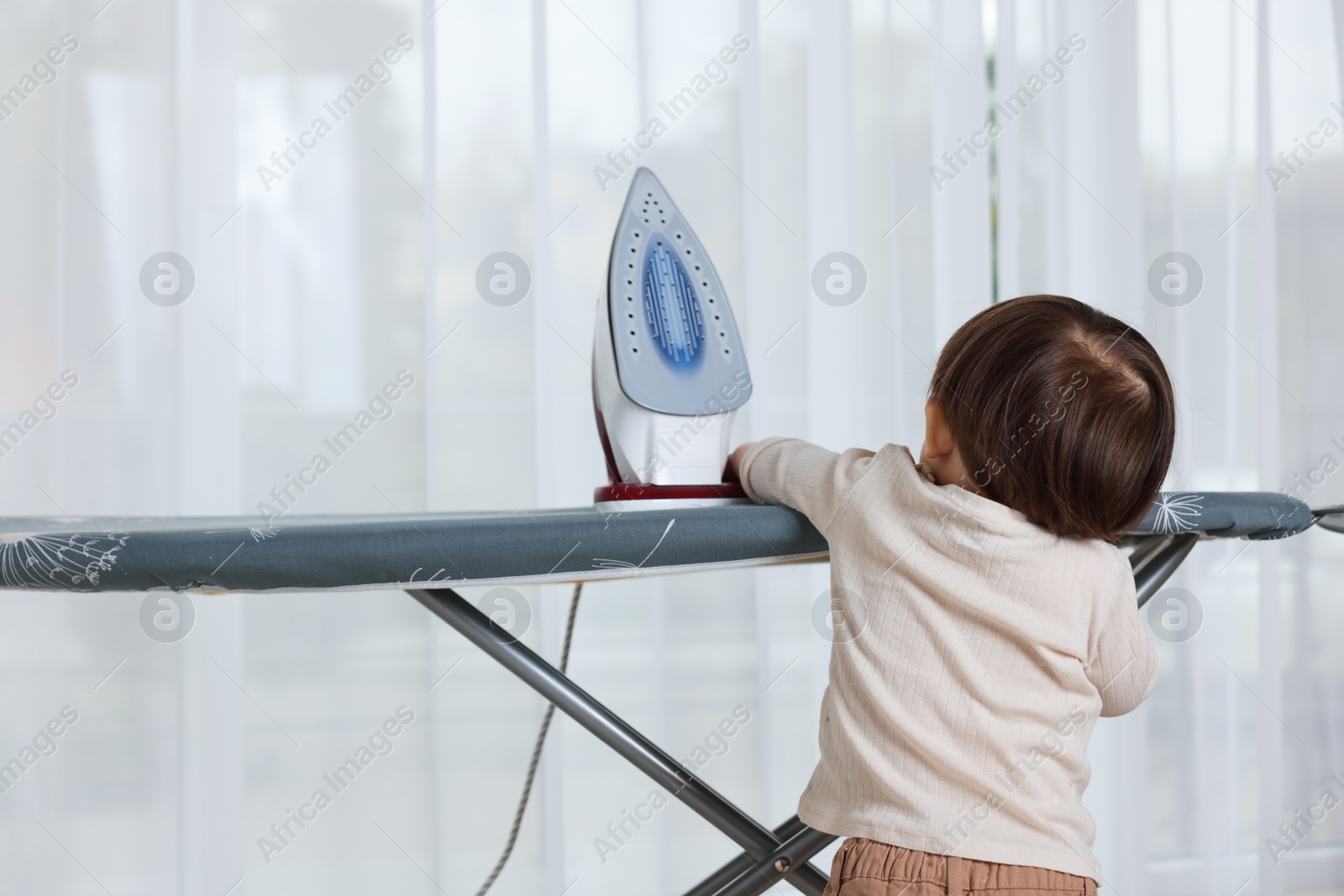 Photo of Little boy looking at iron indoors, back view. Child in danger