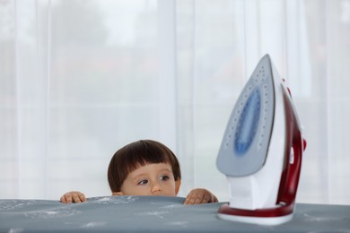 Photo of Little boy looking at iron indoors. Child in danger