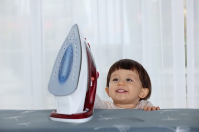 Photo of Smiling boy looking at iron indoors. Child in danger