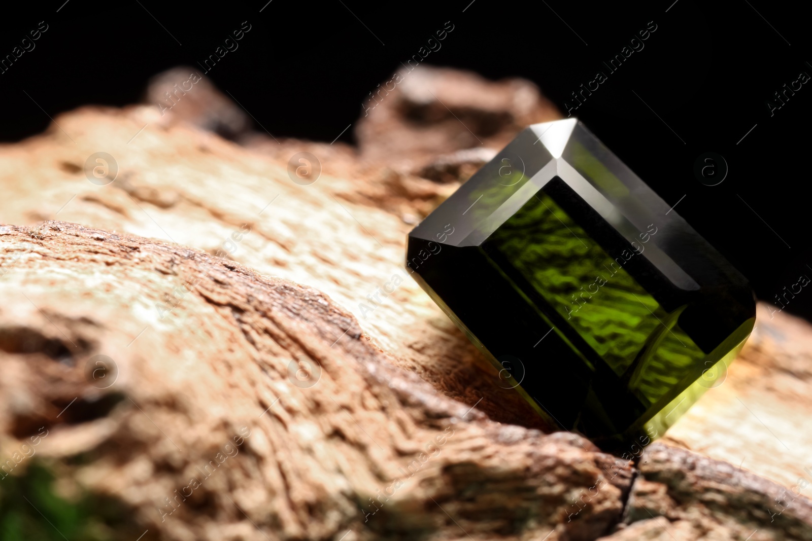 Photo of Beautiful shiny green gemstone on stone, closeup. Space for text