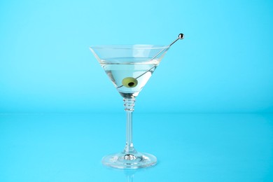 Photo of Martini cocktail with olive in glass on light blue background