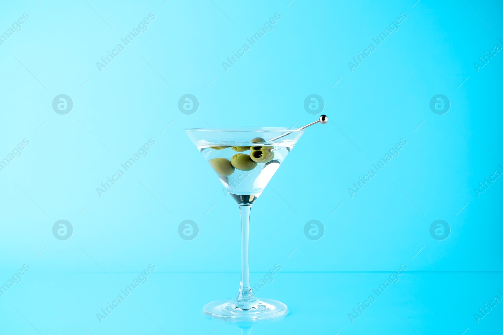 Photo of Martini cocktail with olives in glass on light blue background