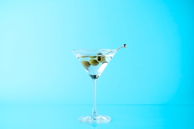 Photo of Martini cocktail with olives in glass on light blue background