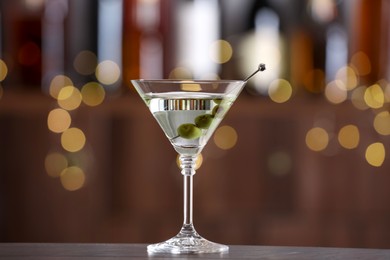 Photo of Martini cocktail with olives in glass on wooden table against blurred background. Bokeh effect