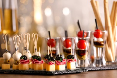 Photo of Many different tasty canapes on wooden table against blurred lights, closeup