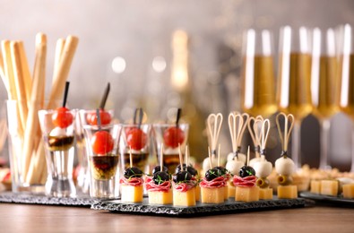 Photo of Many different tasty canapes and wine on wooden table against blurred lights