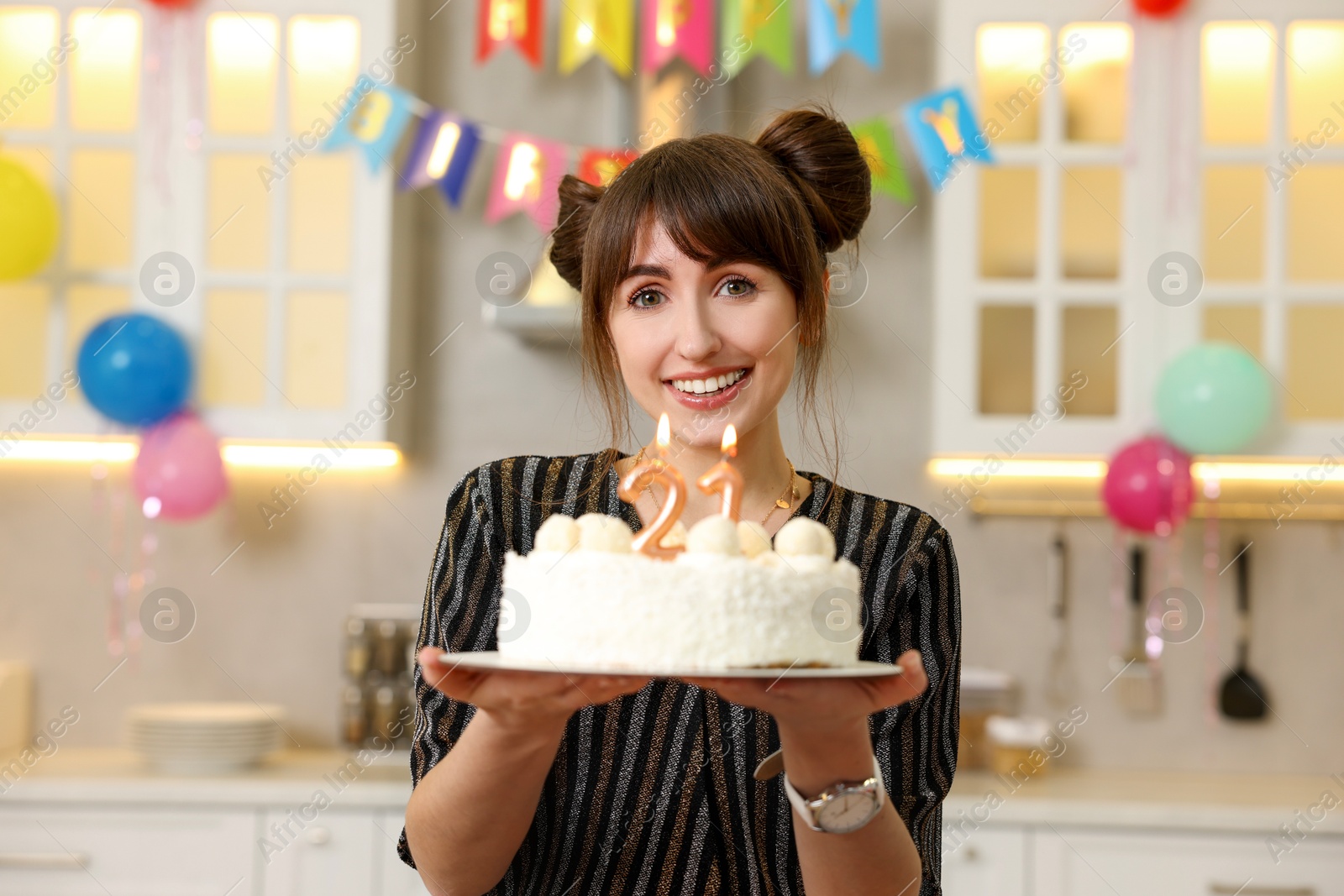 Photo of Coming of age party - 21st birthday. Happy young woman holding tasty cake with number shaped candles at home