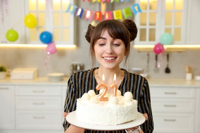 Photo of Coming of age party - 21st birthday. Happy young woman holding tasty cake with number shaped candles at home