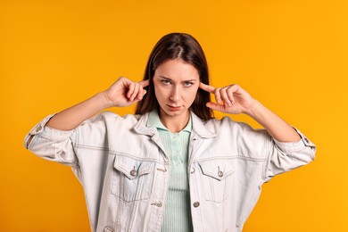 Photo of Annoyed woman covering her ears due to loud sound on orange background