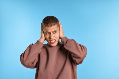 Photo of Annoyed young man covering his ears due to loud sound on light blue background