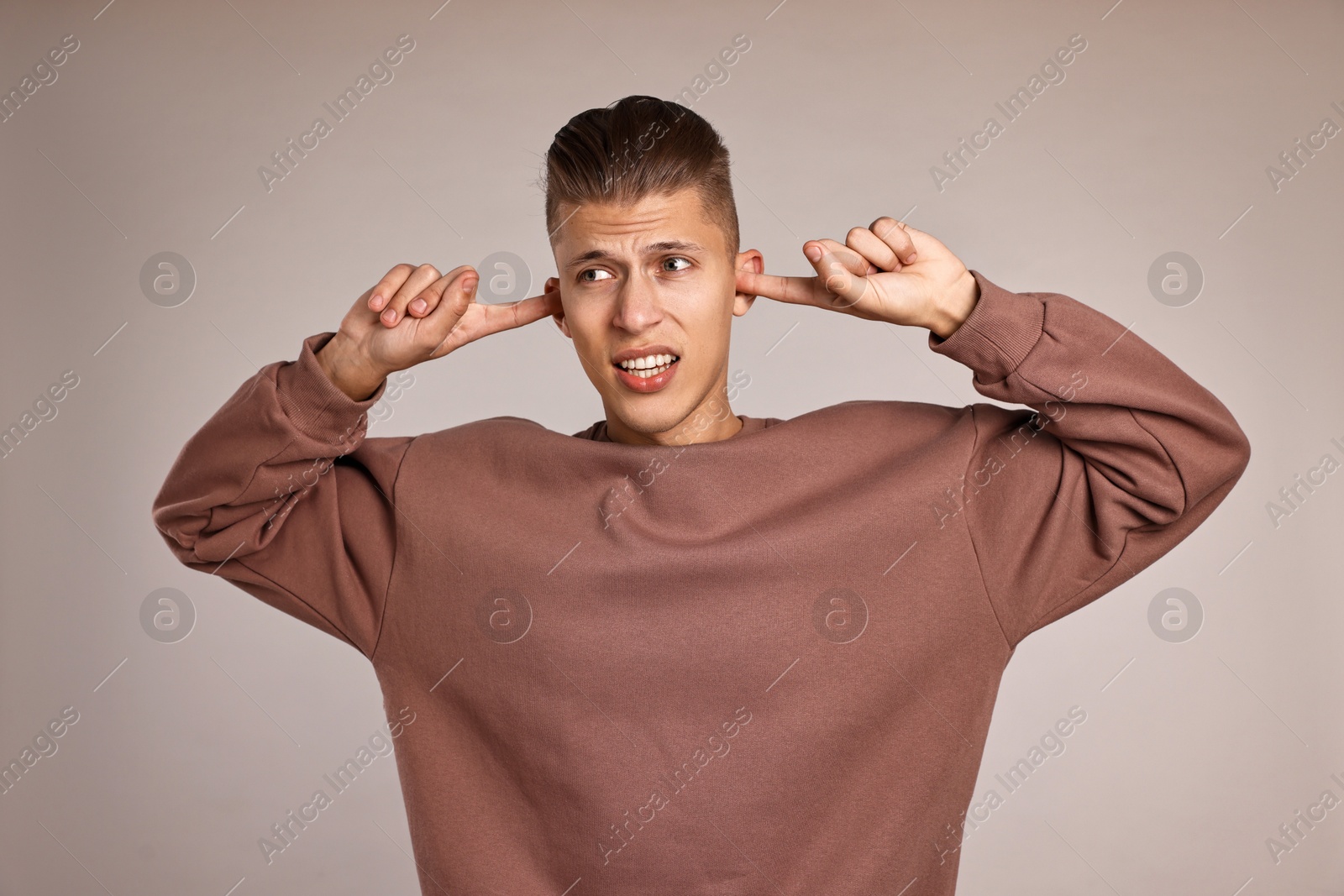 Photo of Annoyed young man covering his ears due to loud sound on light grey background