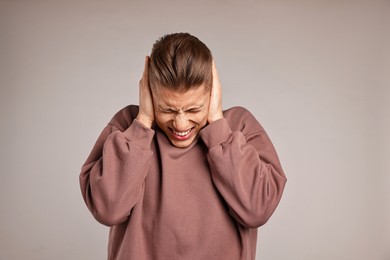 Photo of Annoyed young man covering his ears due to loud sound on light grey background