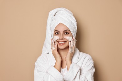 Photo of Beautiful woman washing her face with cleansing foam on beige background