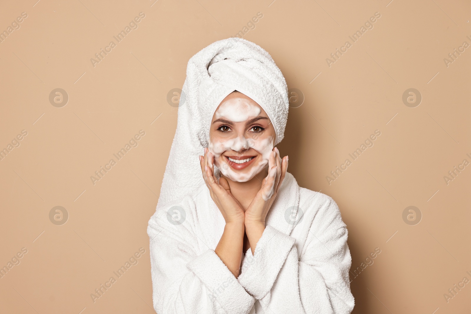 Photo of Beautiful woman washing her face with cleansing foam on beige background