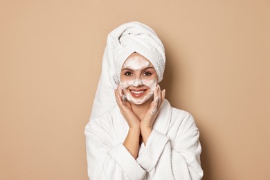 Photo of Beautiful woman washing her face with cleansing foam on beige background