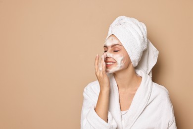 Beautiful woman washing her face with cleansing foam on beige background, space for text