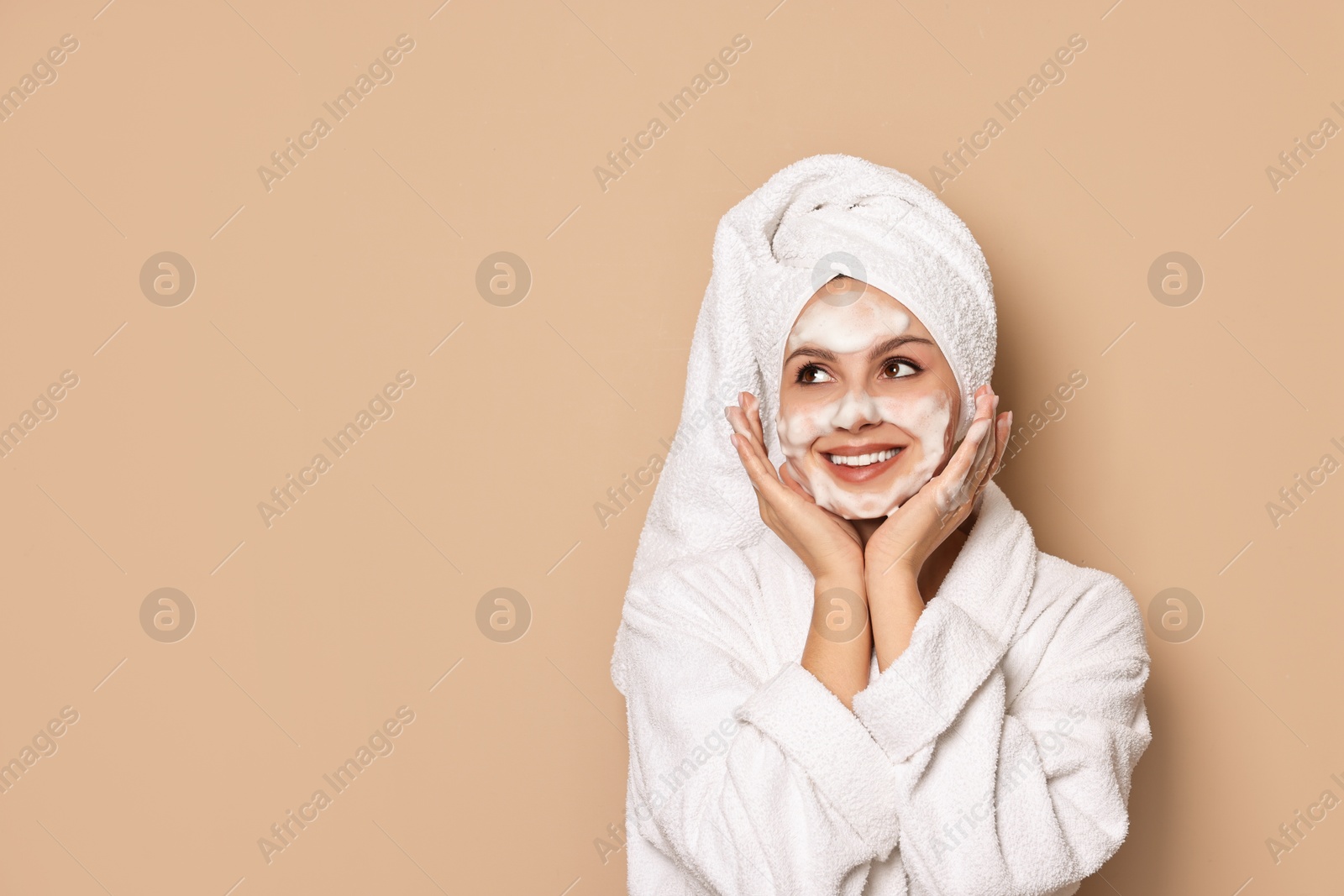 Photo of Beautiful woman washing her face with cleansing foam on beige background, space for text