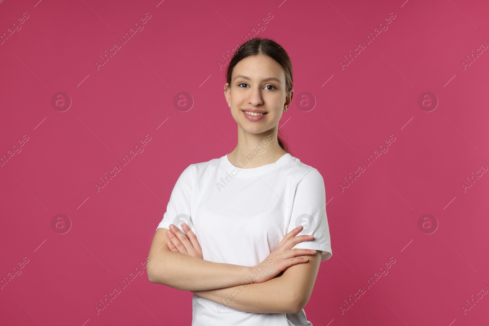 Photo of Portrait of smiling teenage girl with crossed arms on pink background