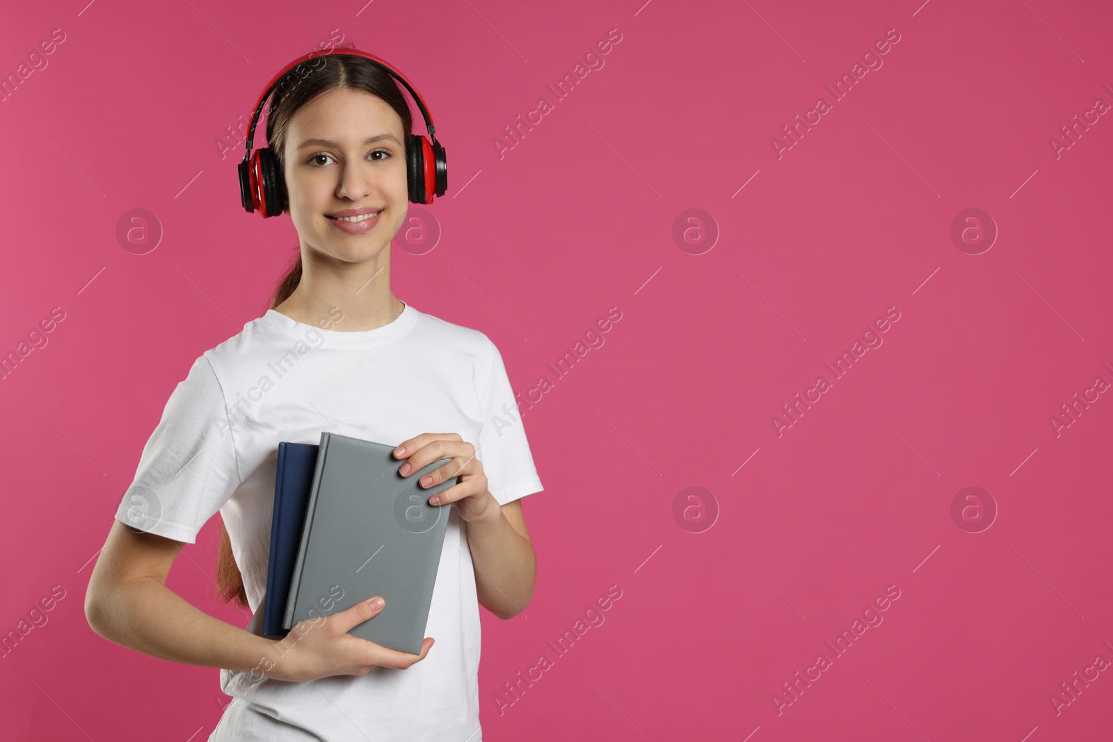 Photo of Portrait of smiling teenage girl with books on pink background. Space for text