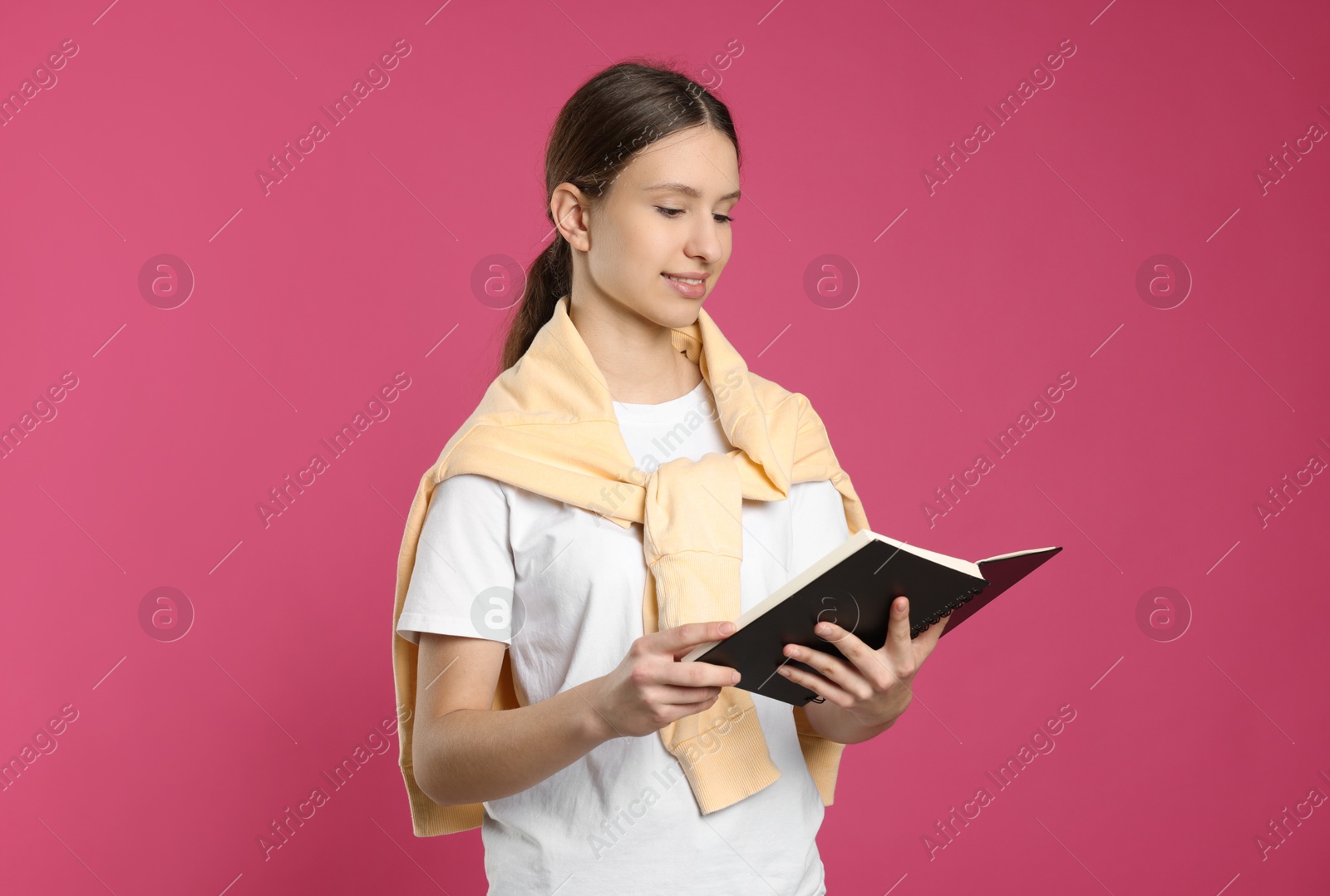 Photo of Portrait of smiling teenage girl reading book on pink background