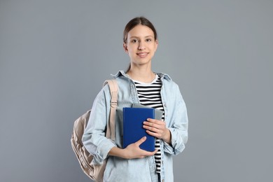 Photo of Portrait of smiling teenage girl with books and backpack on grey background