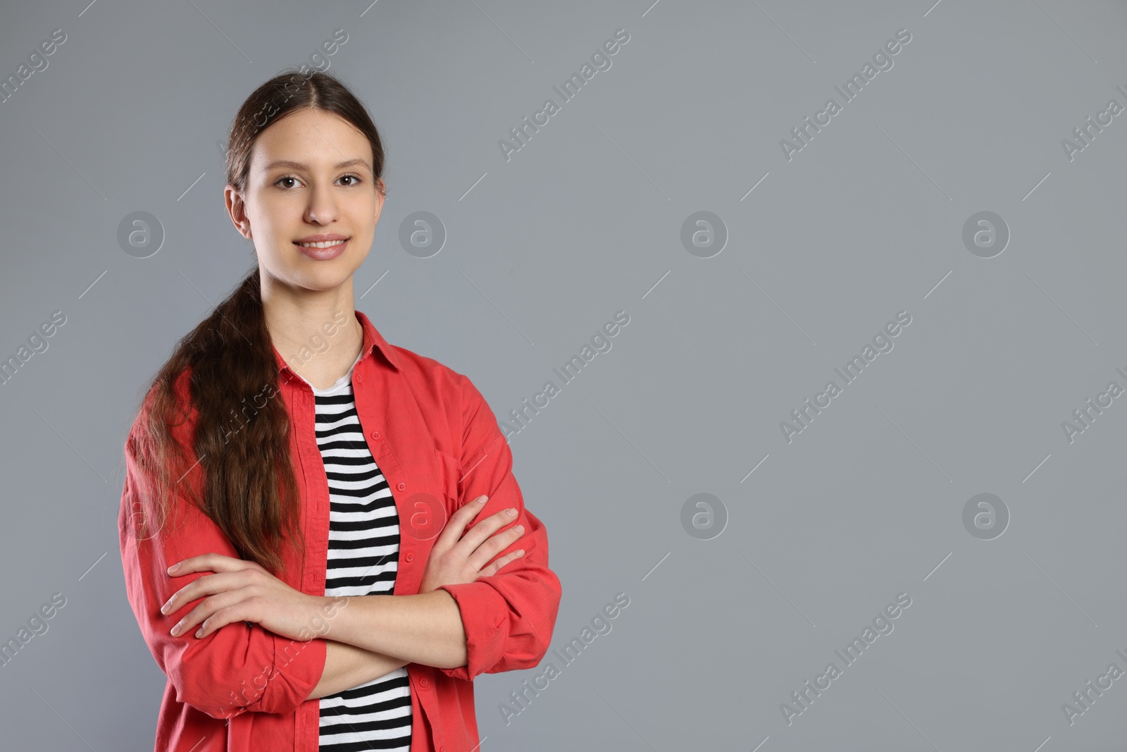 Photo of Portrait of smiling teenage girl with crossed arms on grey background. Space for text