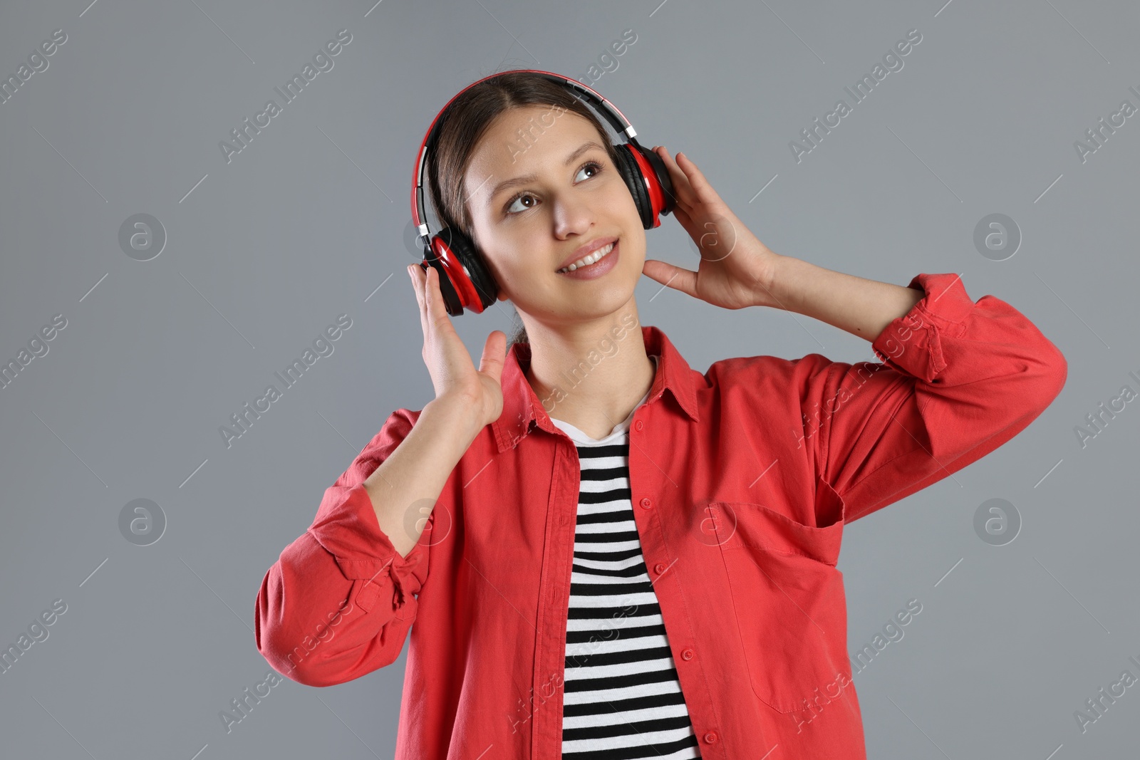 Photo of Portrait of smiling teenage girl in headphones listening to music on grey background