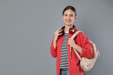 Photo of Portrait of smiling teenage girl with backpack and headphones on grey background. Space for text