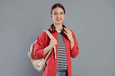 Photo of Portrait of smiling teenage girl with backpack and headphones on grey background