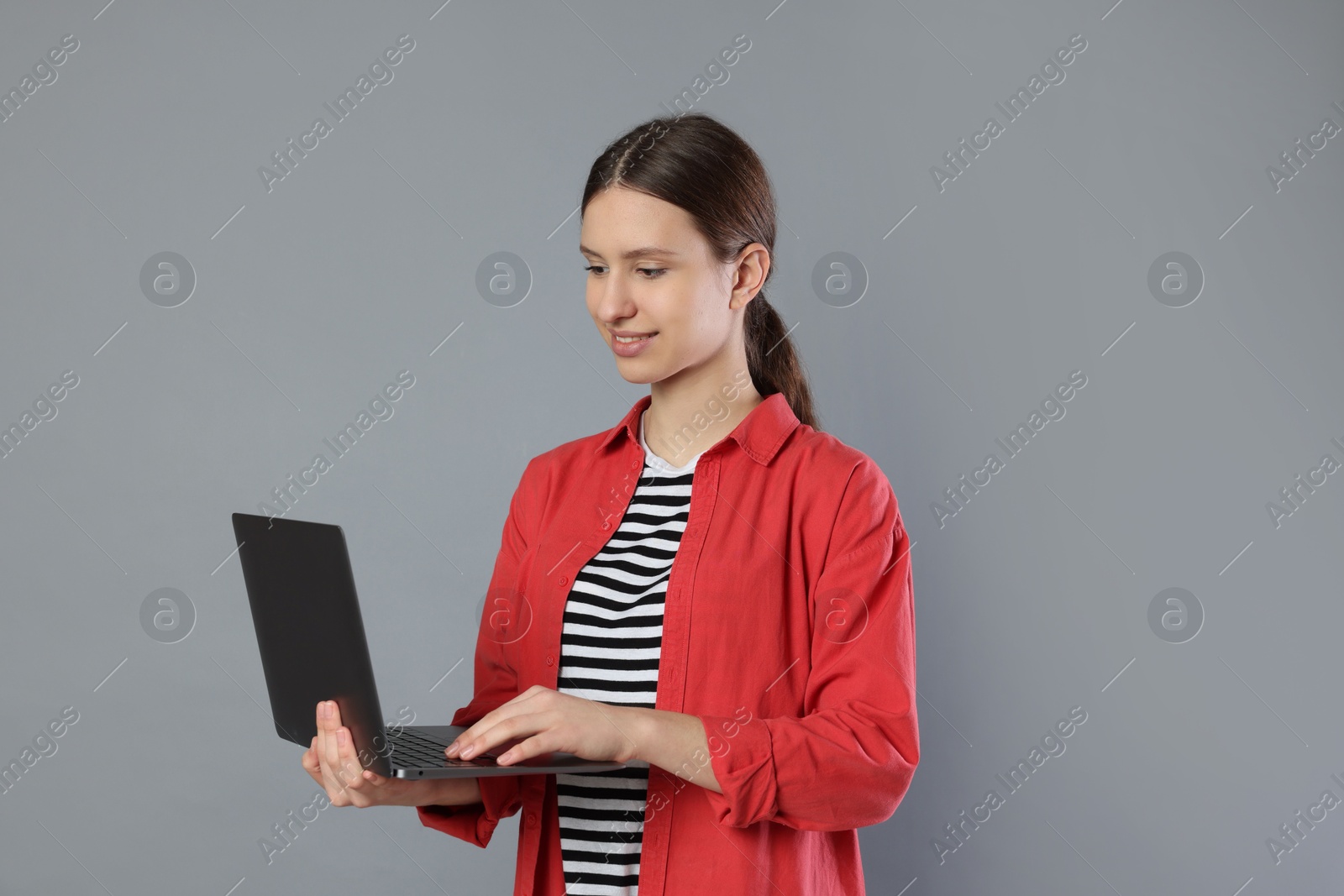 Photo of Portrait of smiling teenage girl with laptop on grey background