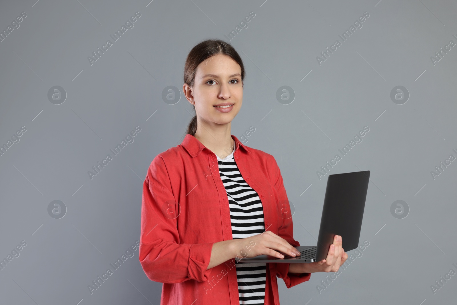 Photo of Portrait of smiling teenage girl with laptop on grey background