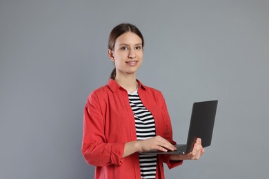 Photo of Portrait of smiling teenage girl with laptop on grey background