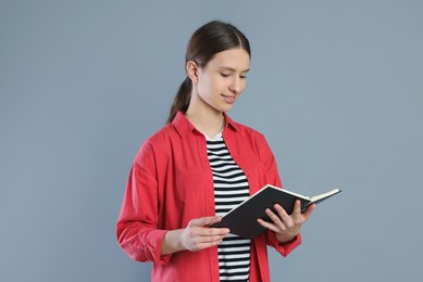 Photo of Portrait of smiling teenage girl reading book on grey background