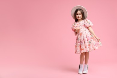 Photo of Stylish little girl wearing oversized high heeled shoes on pink background, space for text