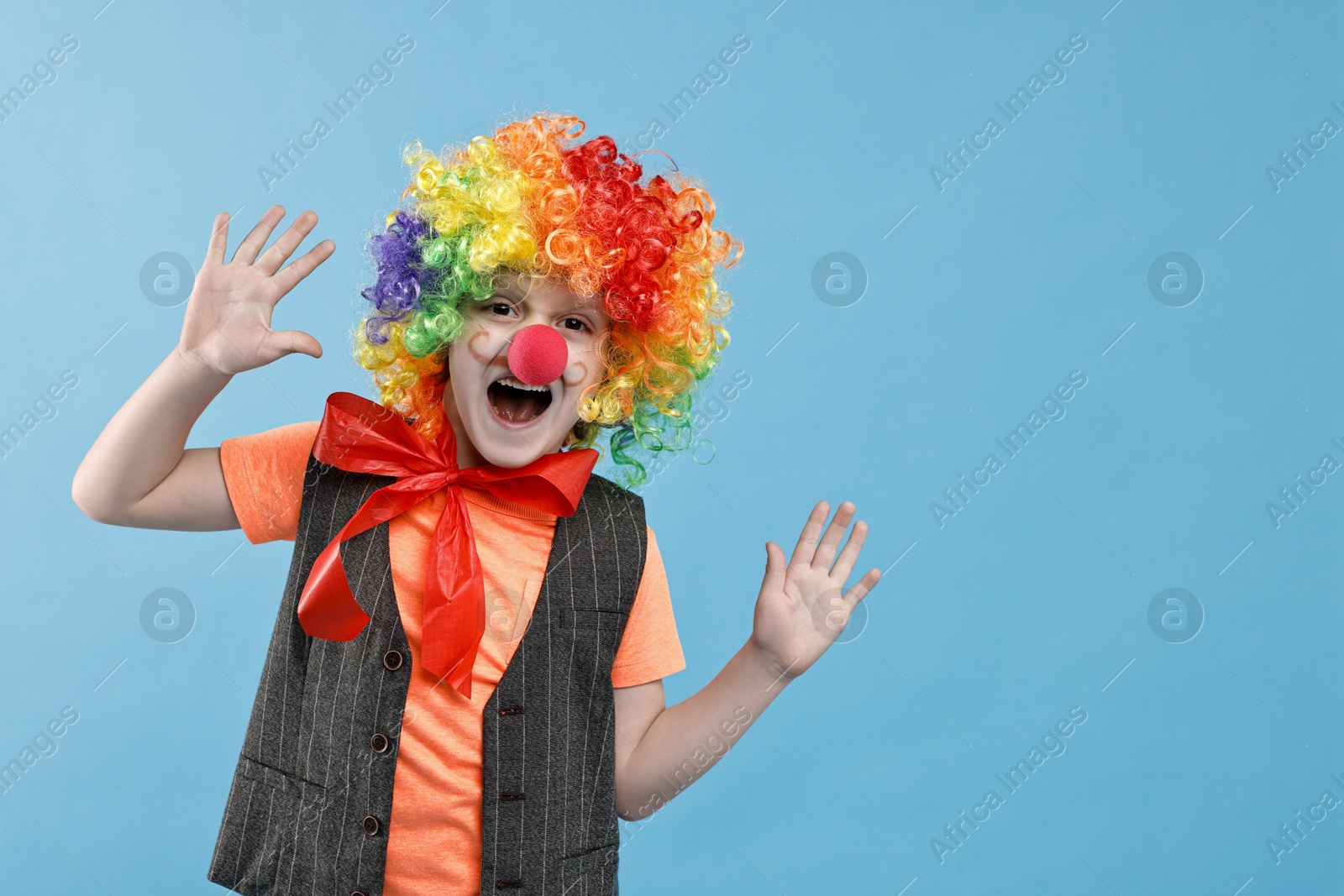 Photo of Little boy dressed like clown on light blue background, space for text. Surprise party