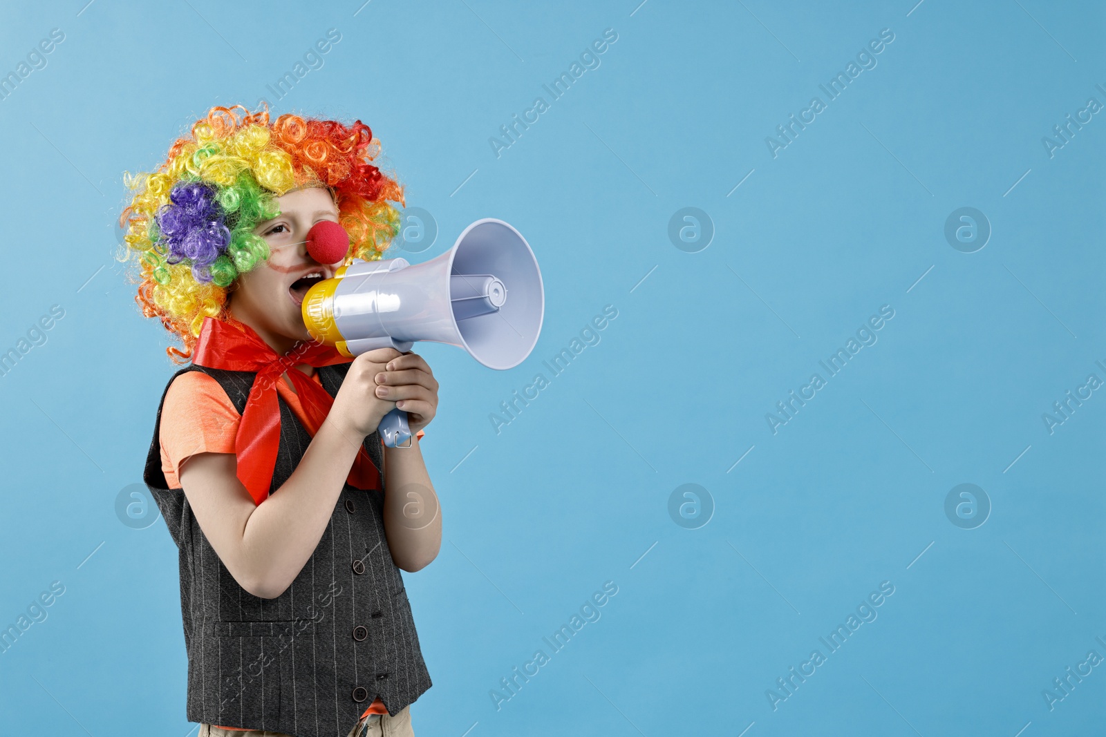 Photo of Little boy dressed like clown shouting in megaphone on light blue background, space for text. Surprise party