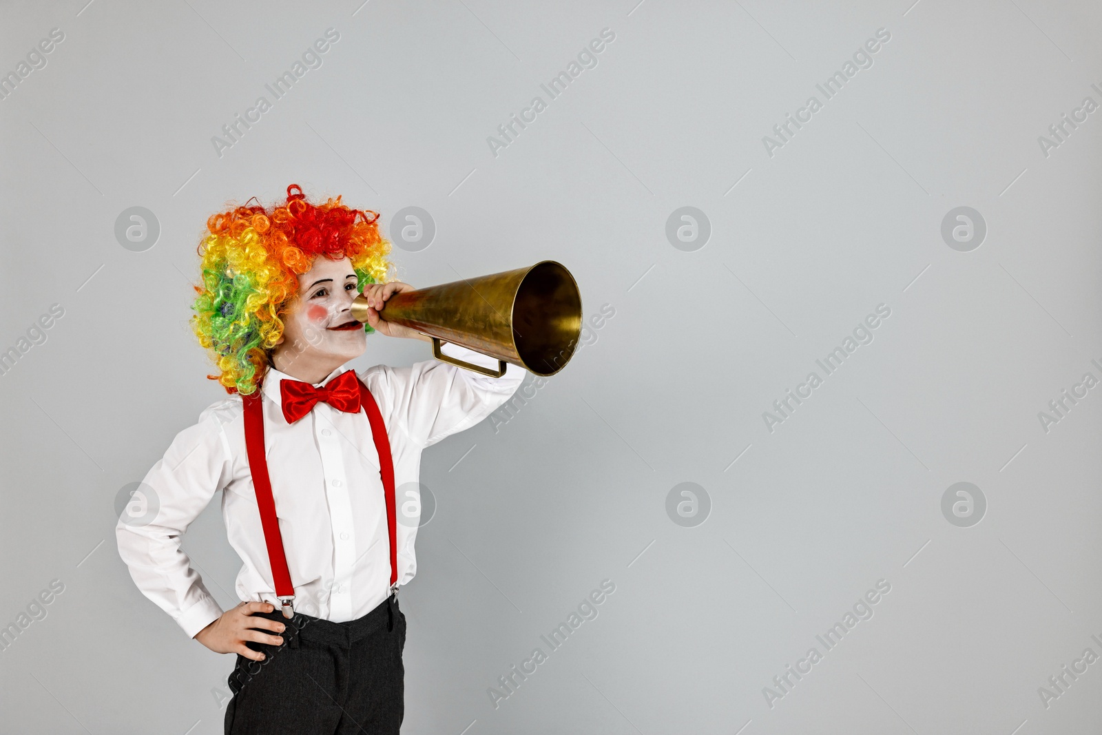 Photo of Little boy dressed like clown with megaphone on grey background, space for text. Surprise party