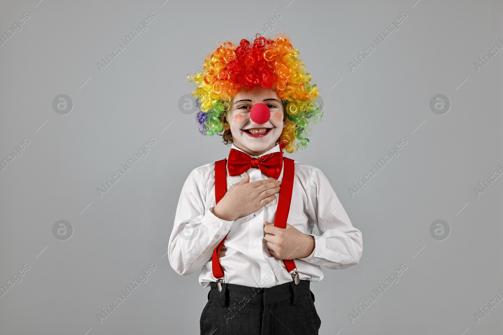 Photo of Happy little boy in clown wig and red nose on grey background. Surprise party