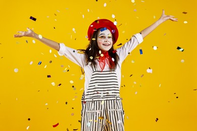 Photo of Happy girl dressed like mime under falling confetti on yellow background. Surprise party