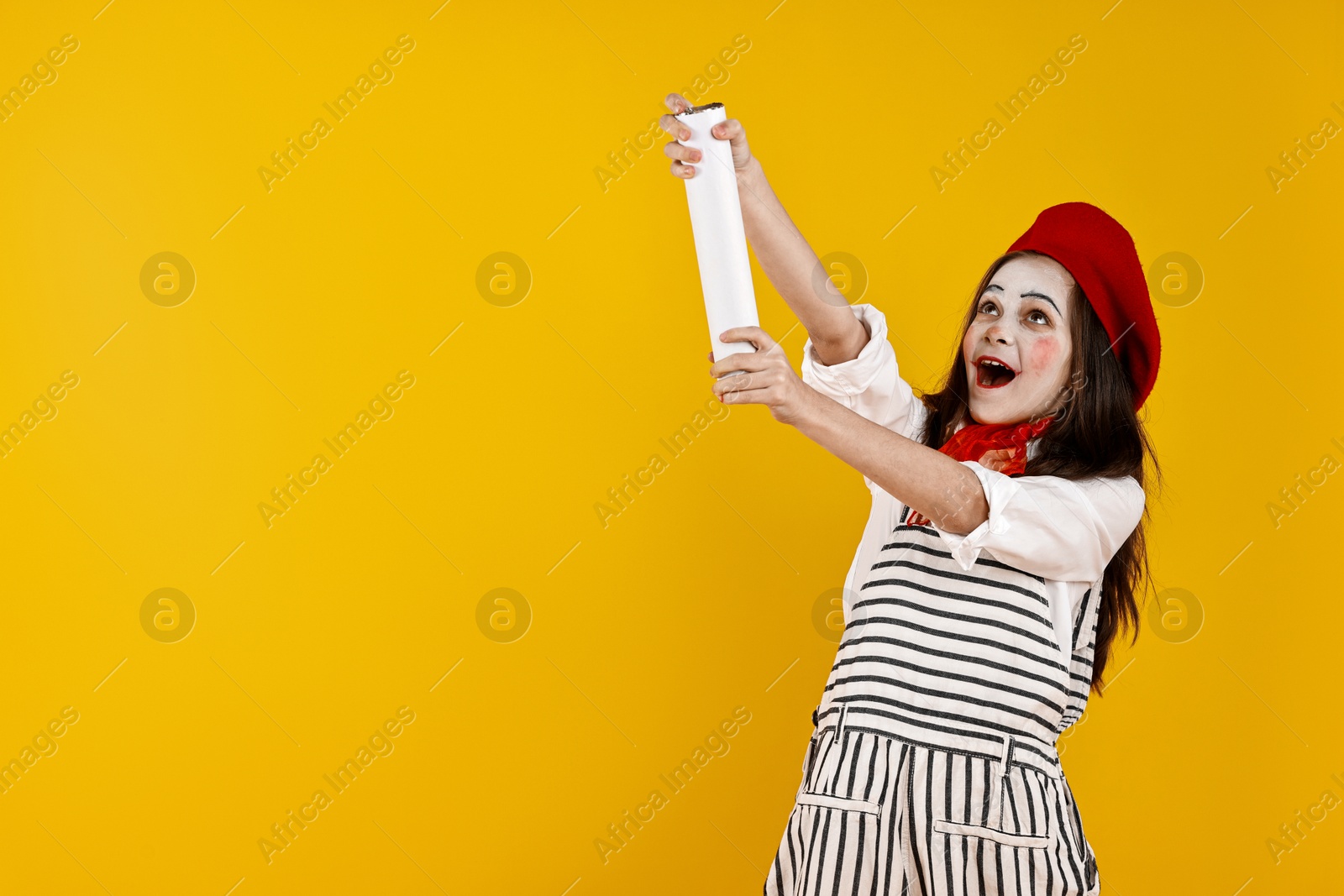 Photo of Happy girl dressed like mime with confetti popper on yellow background, space for text. Surprise party