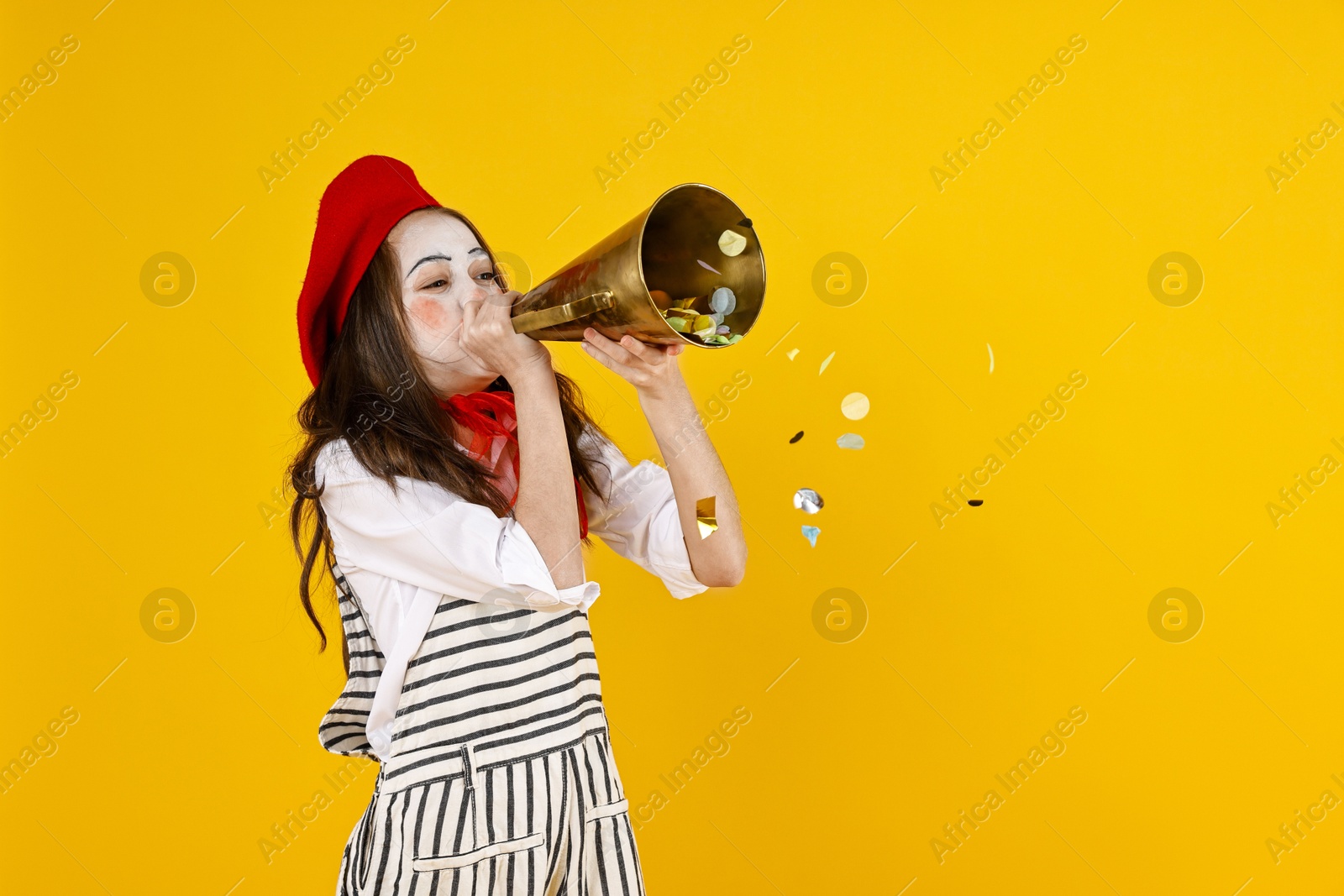 Photo of Happy girl dressed like mime with megaphone and confetti on yellow background, space for text. Surprise party