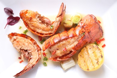 Delicious lobster tails with lemon and green onion on white plate, top view