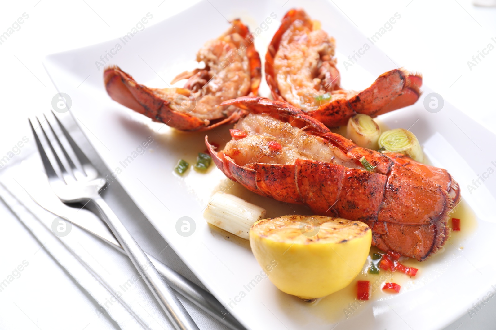 Photo of Delicious lobster tails with lemon and green onion on white table, closeup