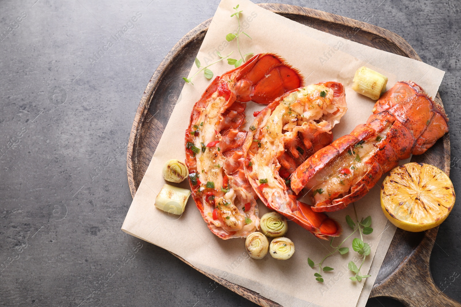 Photo of Delicious lobster tails with lemon, microgreens and green onion on grey textured table, top view. Space for text