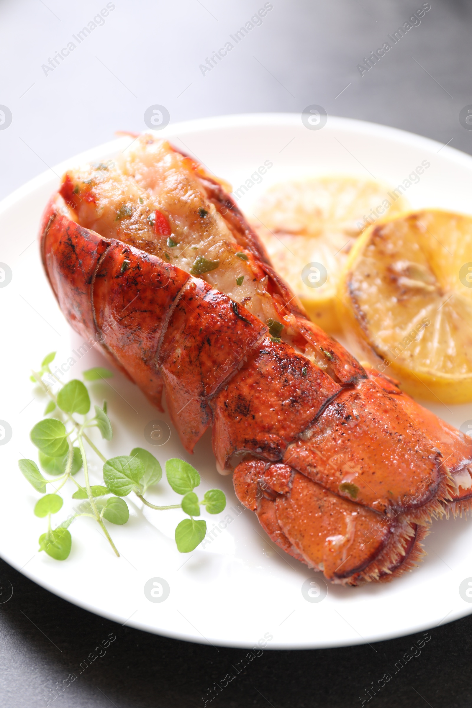 Photo of Delicious lobster tail with microgreens and slices of lemon on grey table, closeup