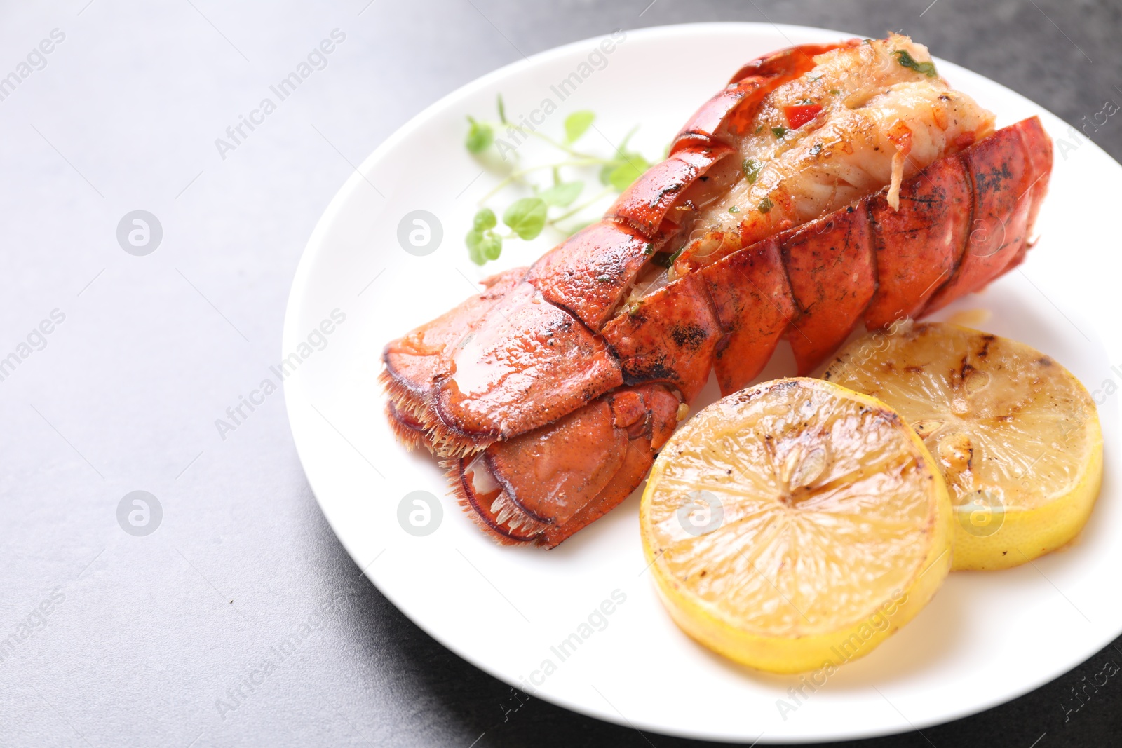 Photo of Delicious lobster tail with microgreens and slices of lemon on grey textured table, closeup