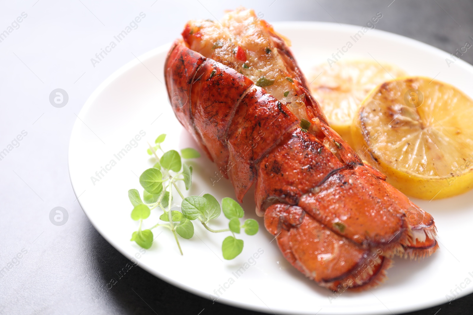 Photo of Delicious lobster tail with microgreens and slices of lemon on grey textured table, closeup